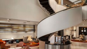 A modern lobby with a curved staircase, seating areas, and a reception desk. - ibis Sharq Kuwait (Kuwait City)