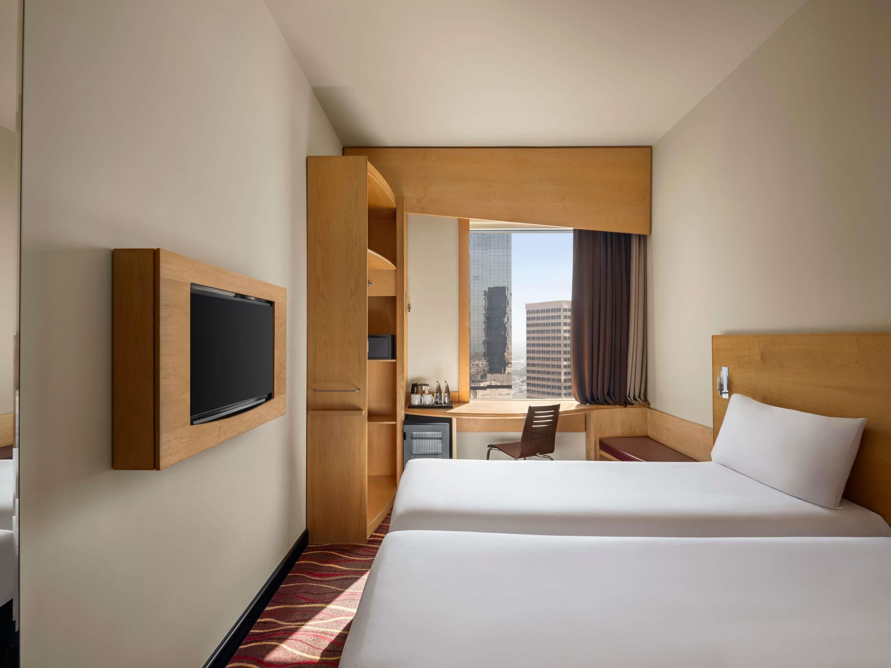 Una habitación de hotel con cama, escritorio, televisor y ventana con vista a la ciudad.