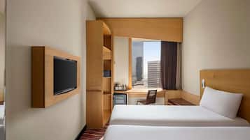 A hotel room with a bed, a desk, a TV, and a window with a city view.