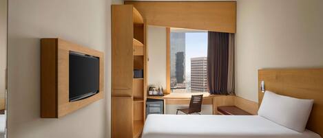 Una habitación de hotel con cama, escritorio, televisor y ventana con vista a la ciudad.