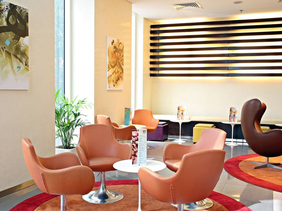 A modern lobby with orange chairs, a coffee machine, and artwork on the walls.