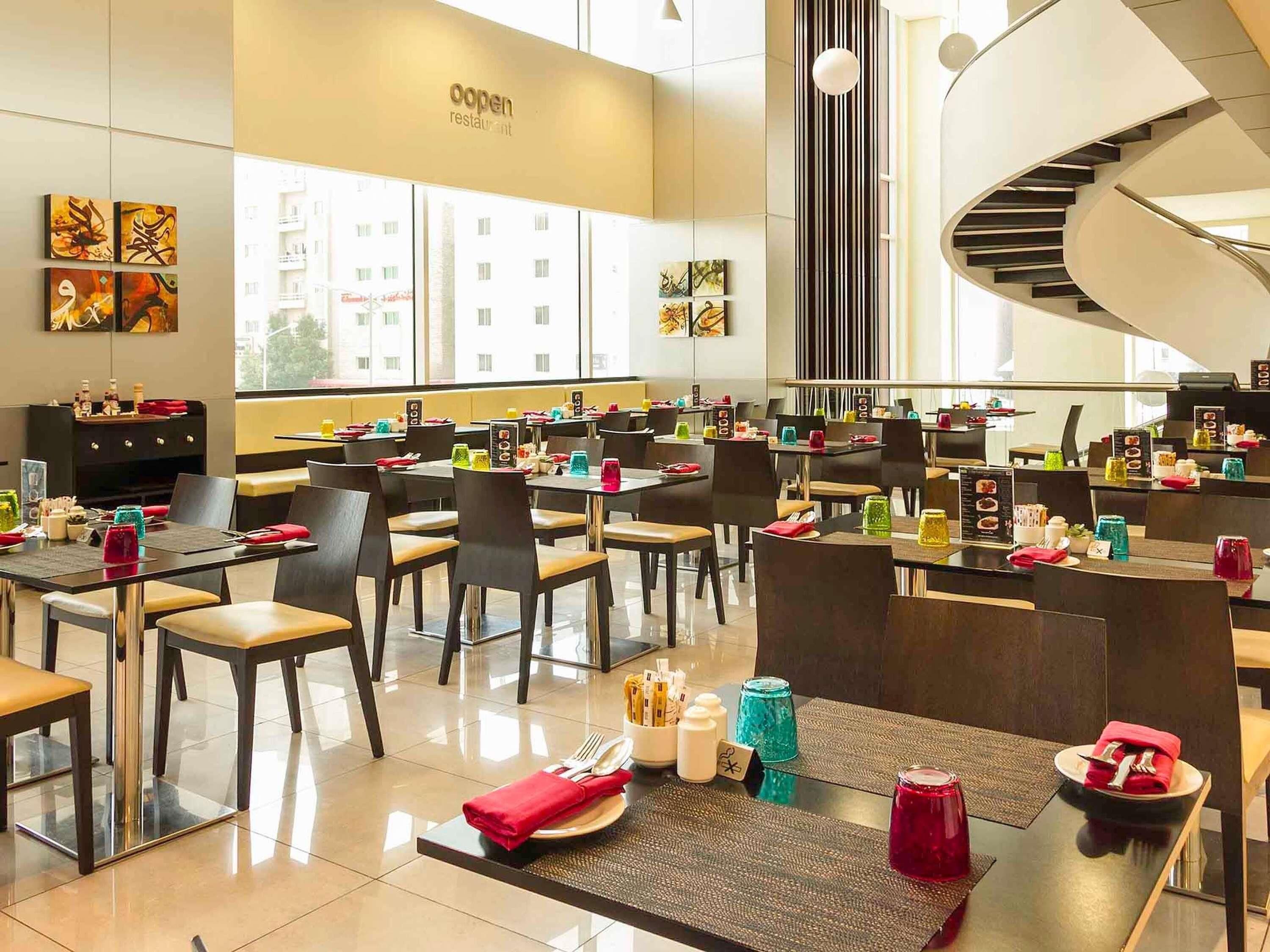A modern restaurant with a central spiral staircase, multiple dining tables, and artwork on the walls.