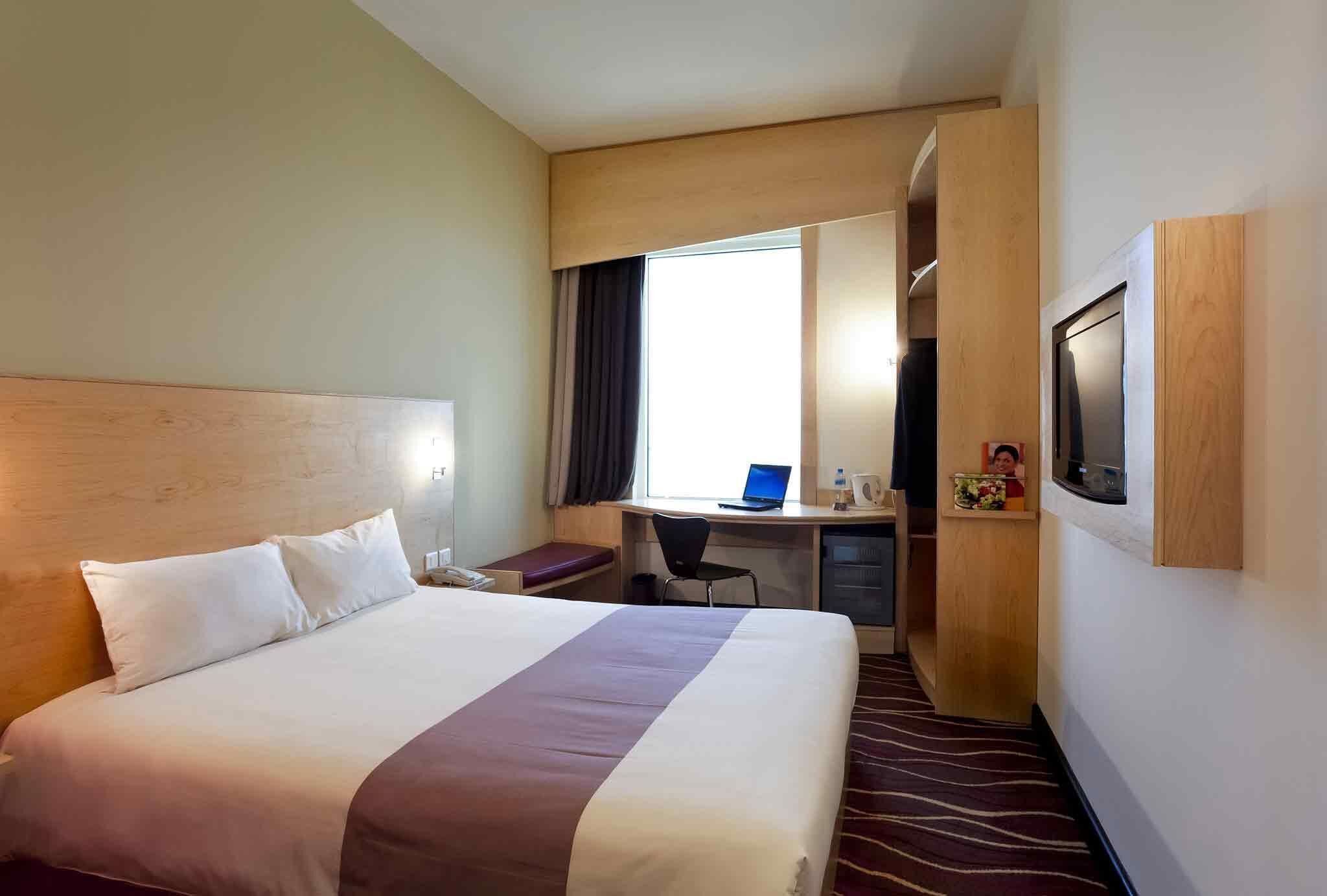 Een hotelkamer met een groot bed, een bureau met een laptop, een televisie en een douchehoek.