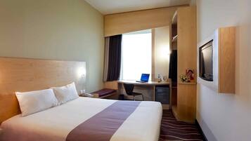 Een hotelkamer met een groot bed, een bureau met een laptop, een televisie en een douchehoek.