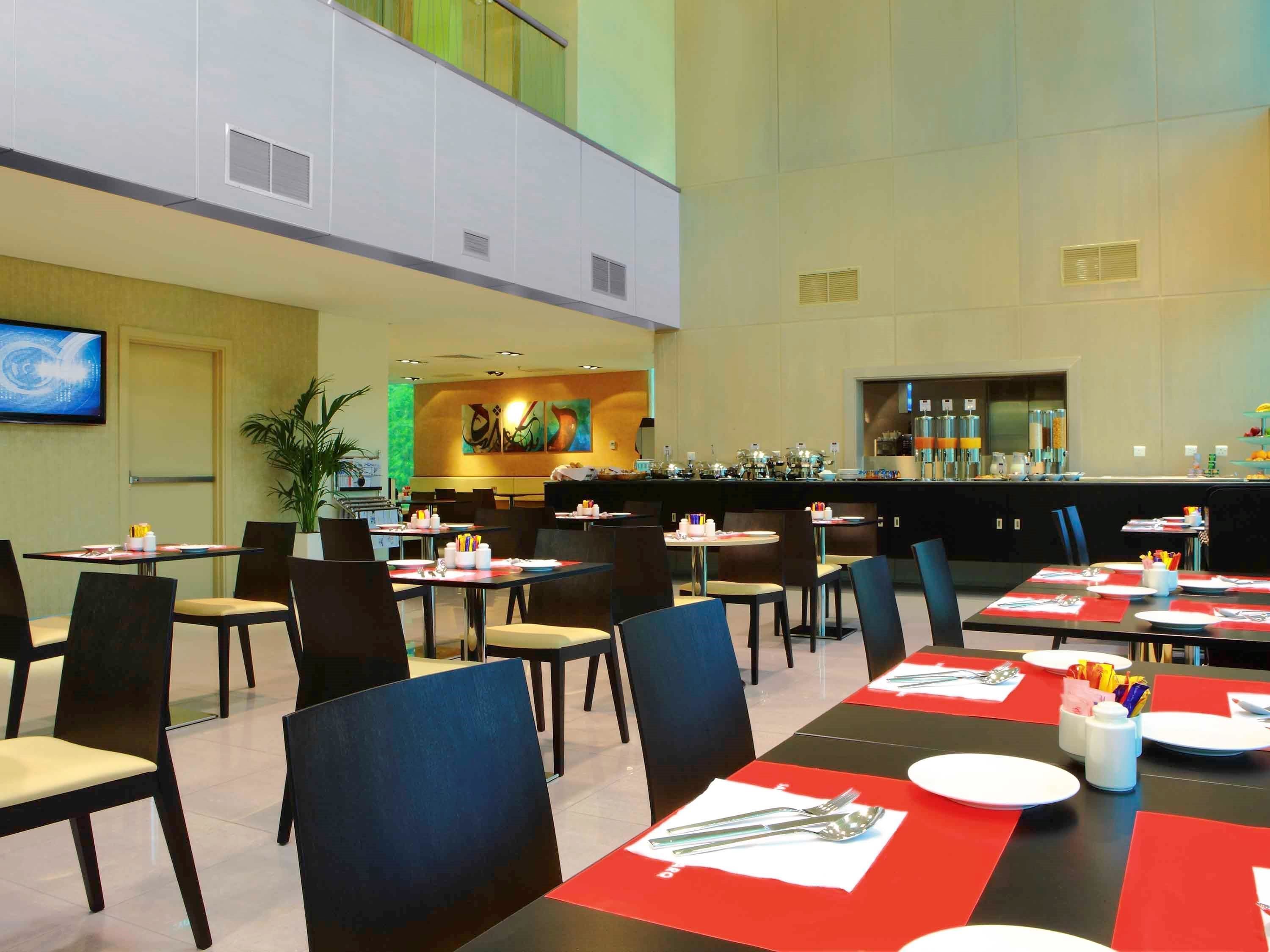 A modern dining area with multiple tables and chairs, a bar area, and a large screen on the wall.