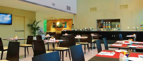 Uma sala de jantar moderna com várias mesas e cadeiras, um bar e uma tela grande na parede.