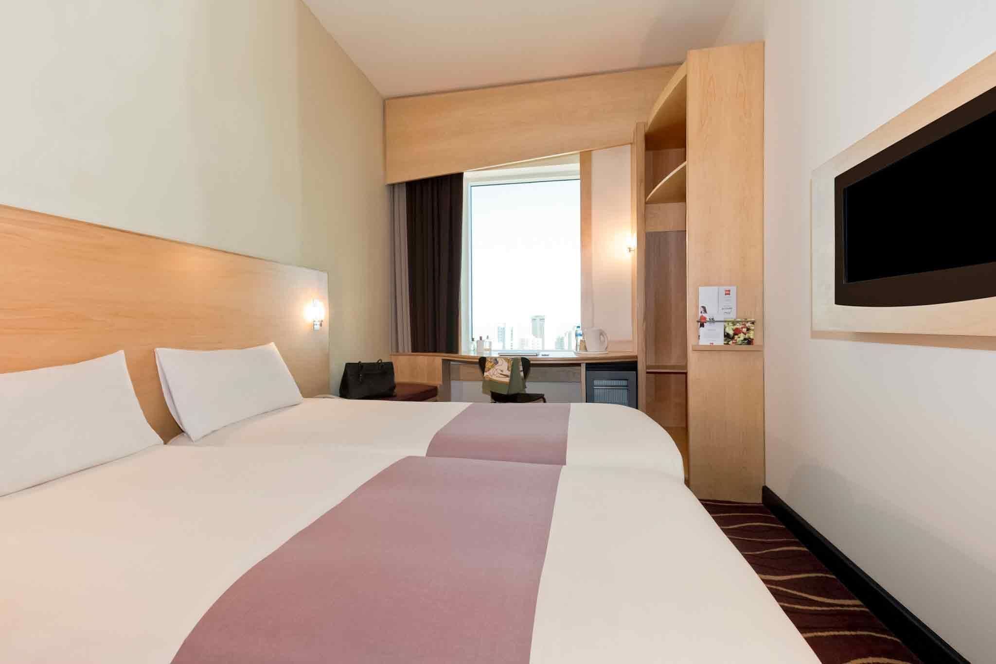 A hotel room with a large bed, a desk, a chair, a TV, and a window.