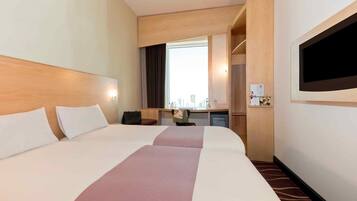 A hotel room with a large bed, a desk, a chair, a TV, and a window.