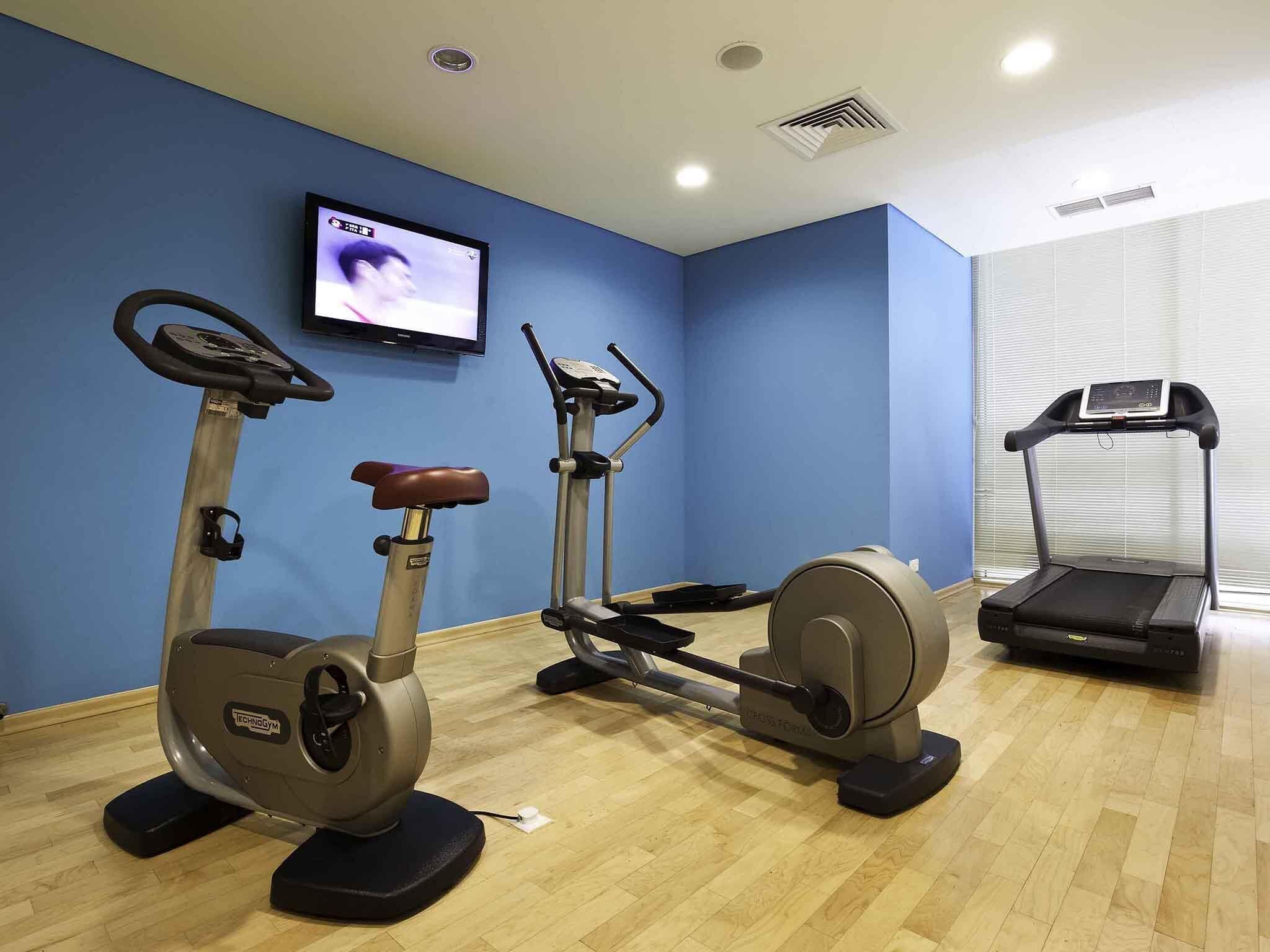 Un gimnasio con equipo cardiovascular, un televisor y una cinta de correr.