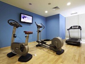 Une salle de remise en forme équipée d’appareils de cardio, d’un téléviseur et d’un tapis de course.