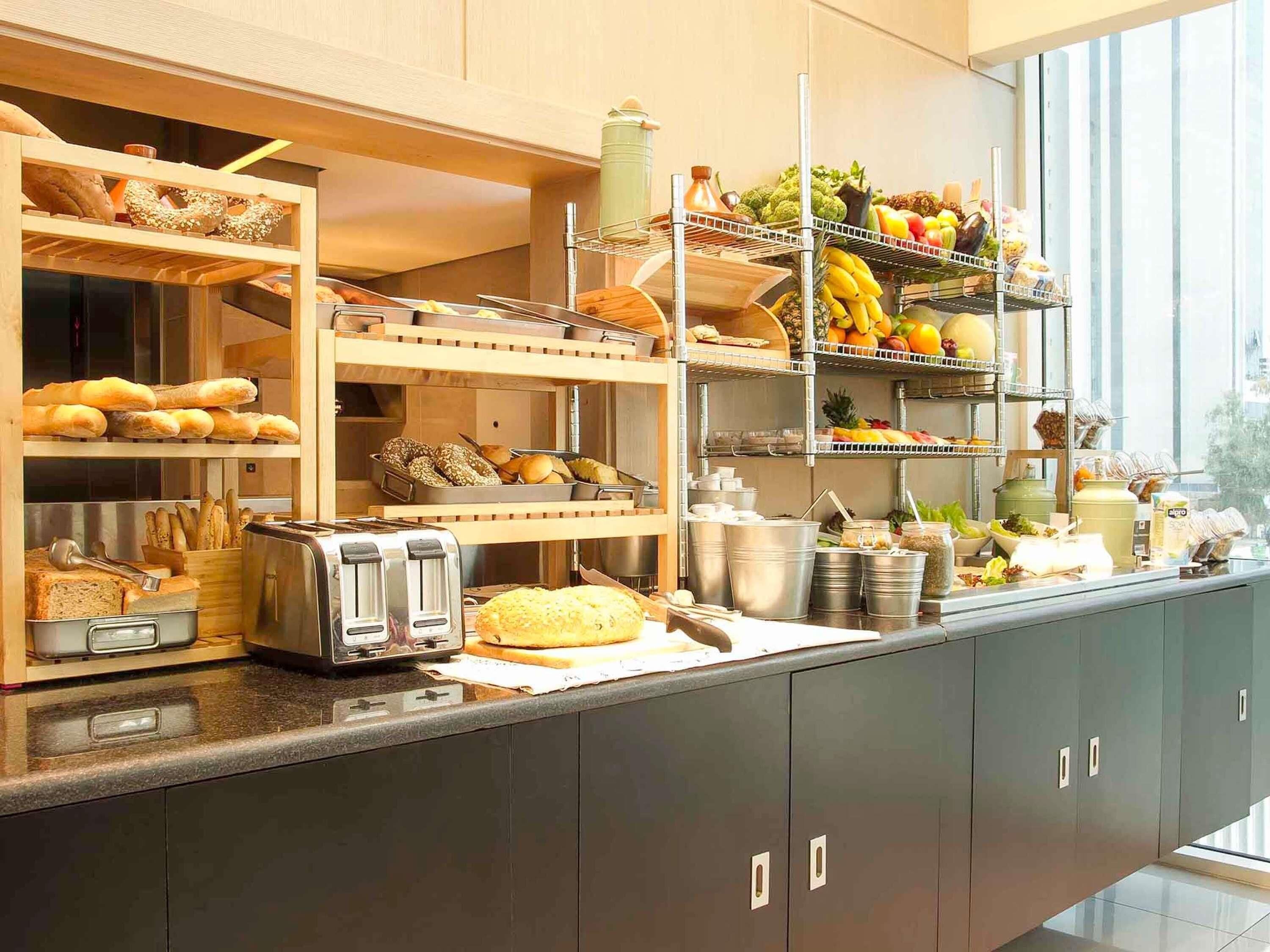 A breakfast buffet with various breads, pastries, fruits, and beverages.