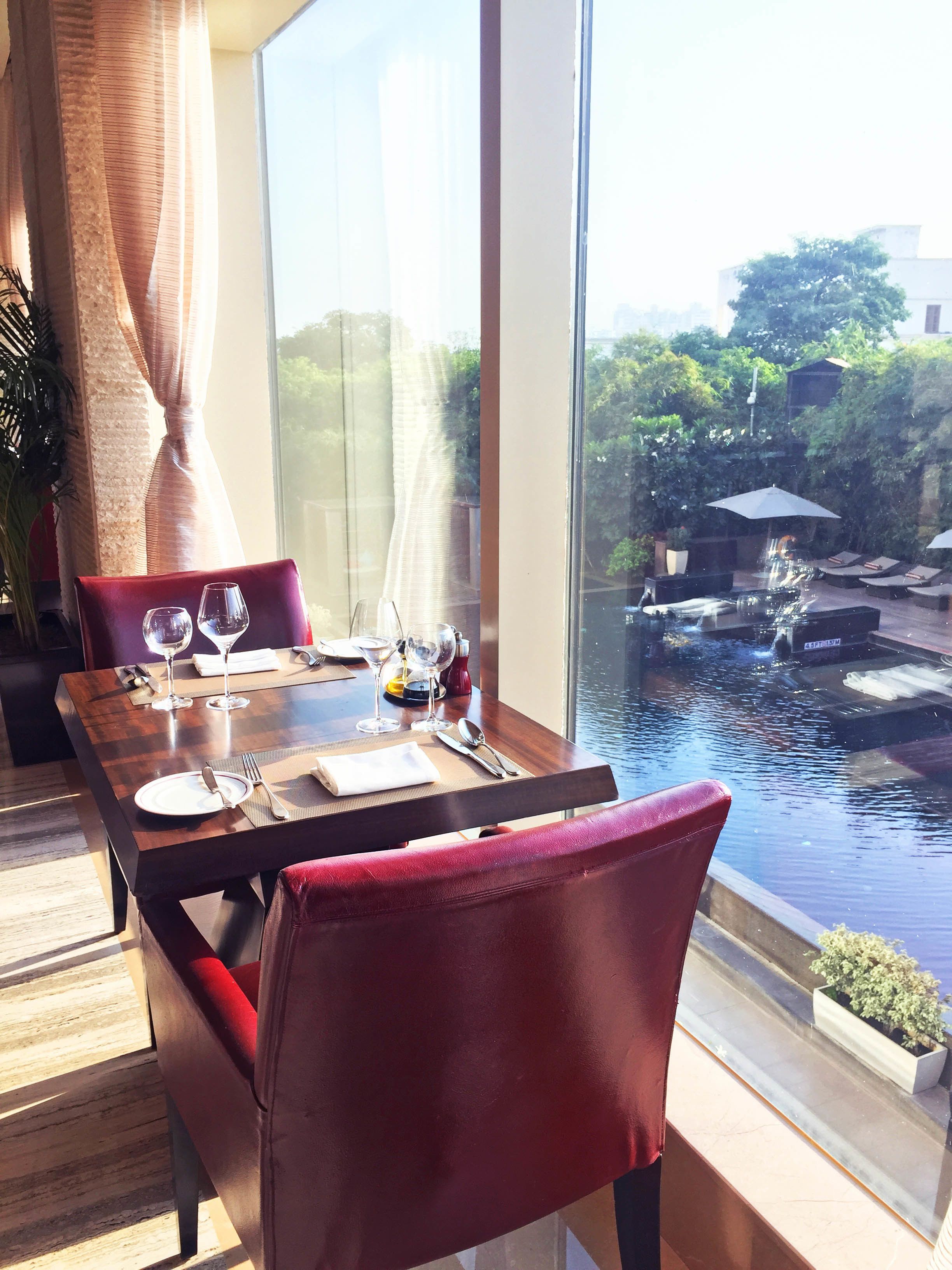 A dining area with a table set for two, overlooking a water feature and greenery.