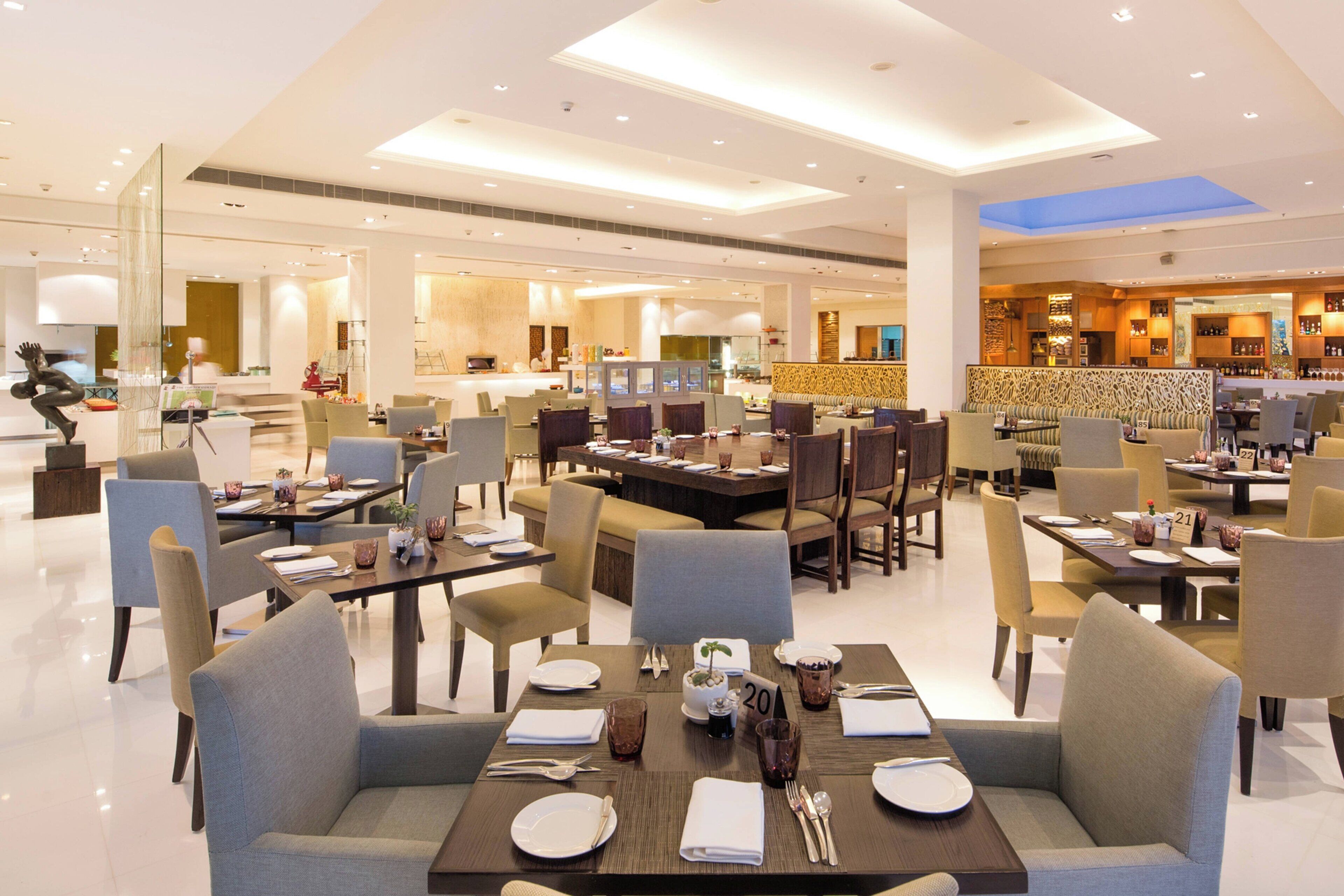 A spacious hotel lobby with multiple dining areas, each equipped with tables, chairs, and modern decor.