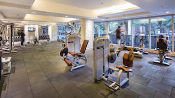A gym with various exercise machines, a television, and a large window providing a view of the outdoors.
