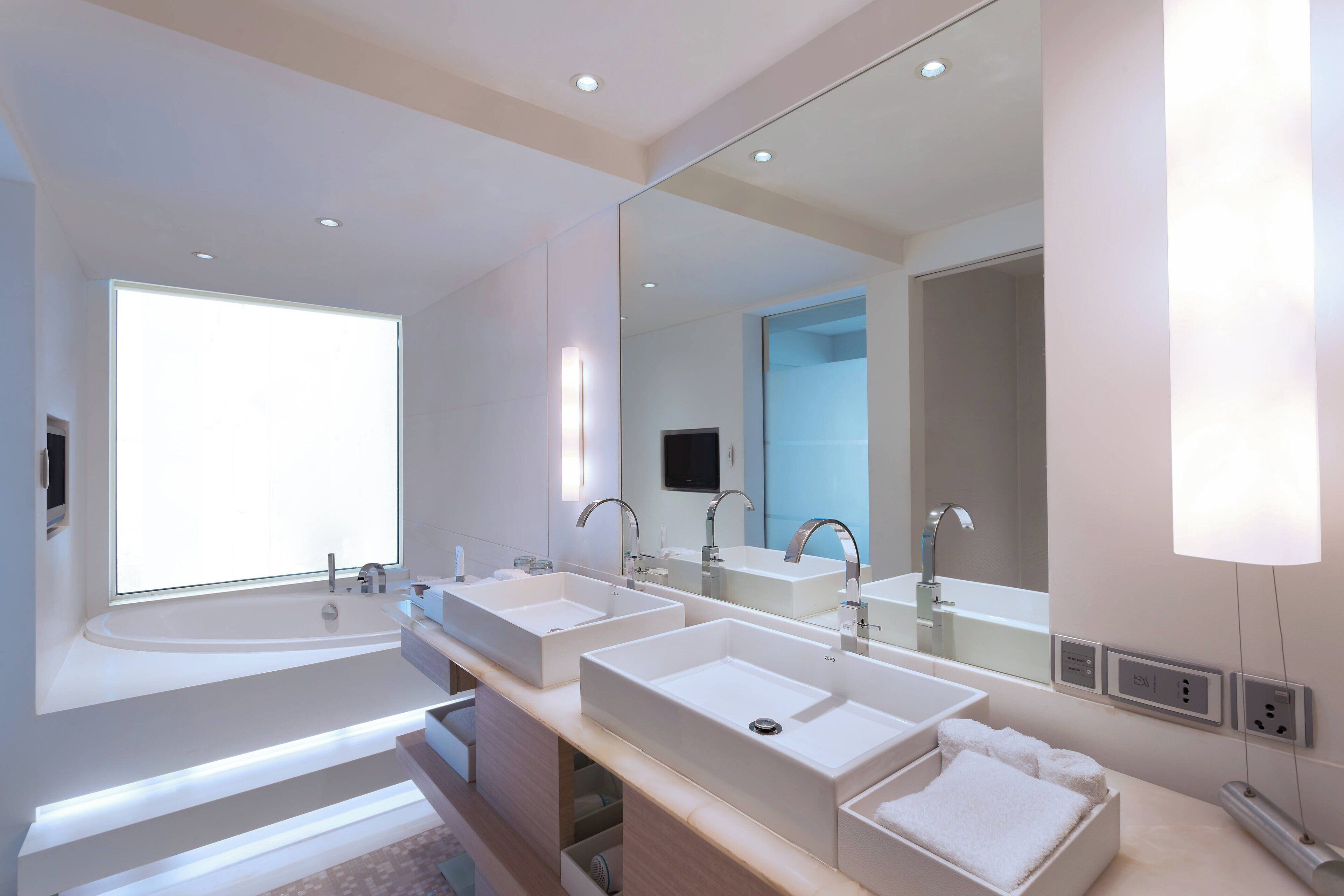 A modern bathroom with three sinks, a large mirror, and a bathtub.