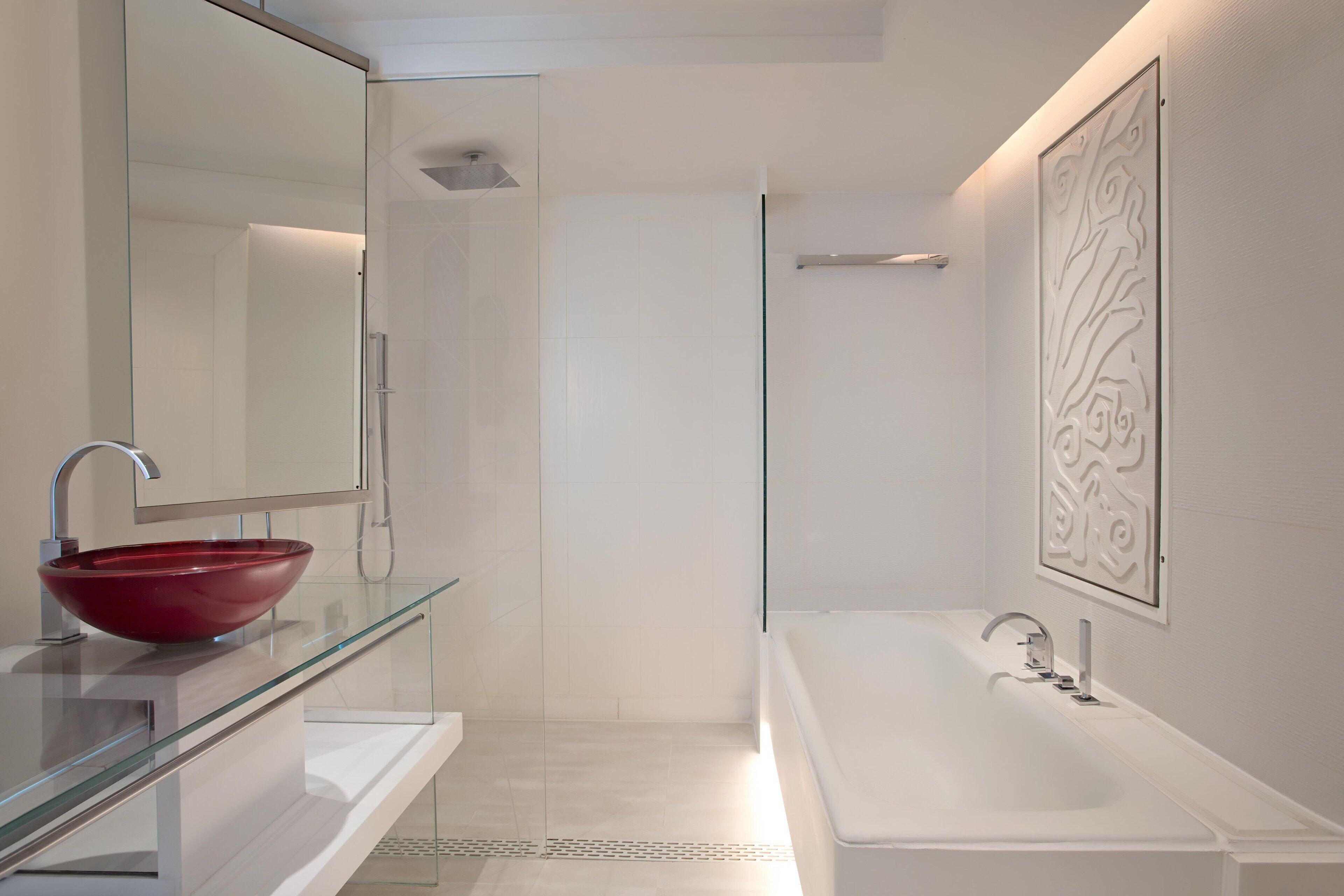 A modern bathroom with a glass-enclosed shower, a red vessel sink, and a large white bathtub.