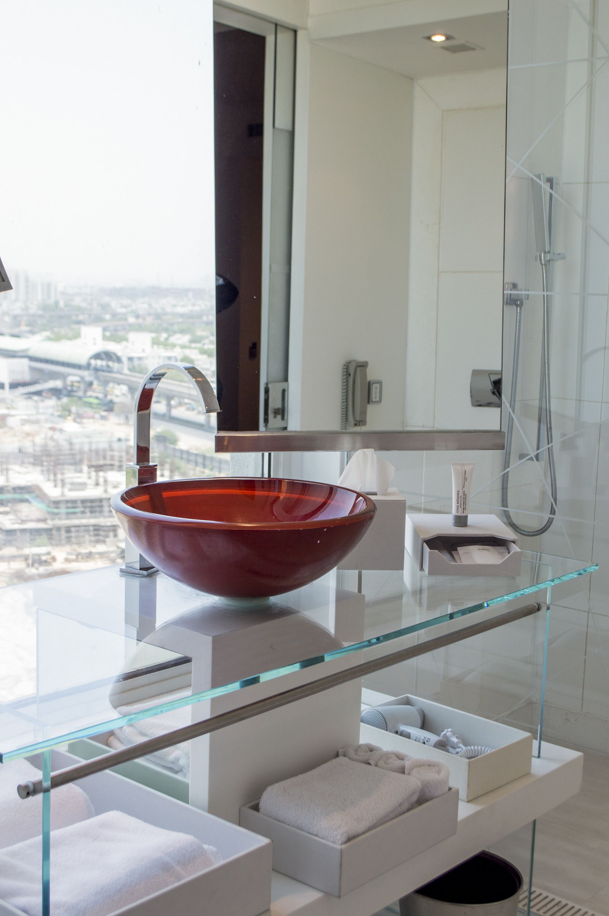 A modern bathroom with a large glass sink, a glass shower enclosure, and a city view.