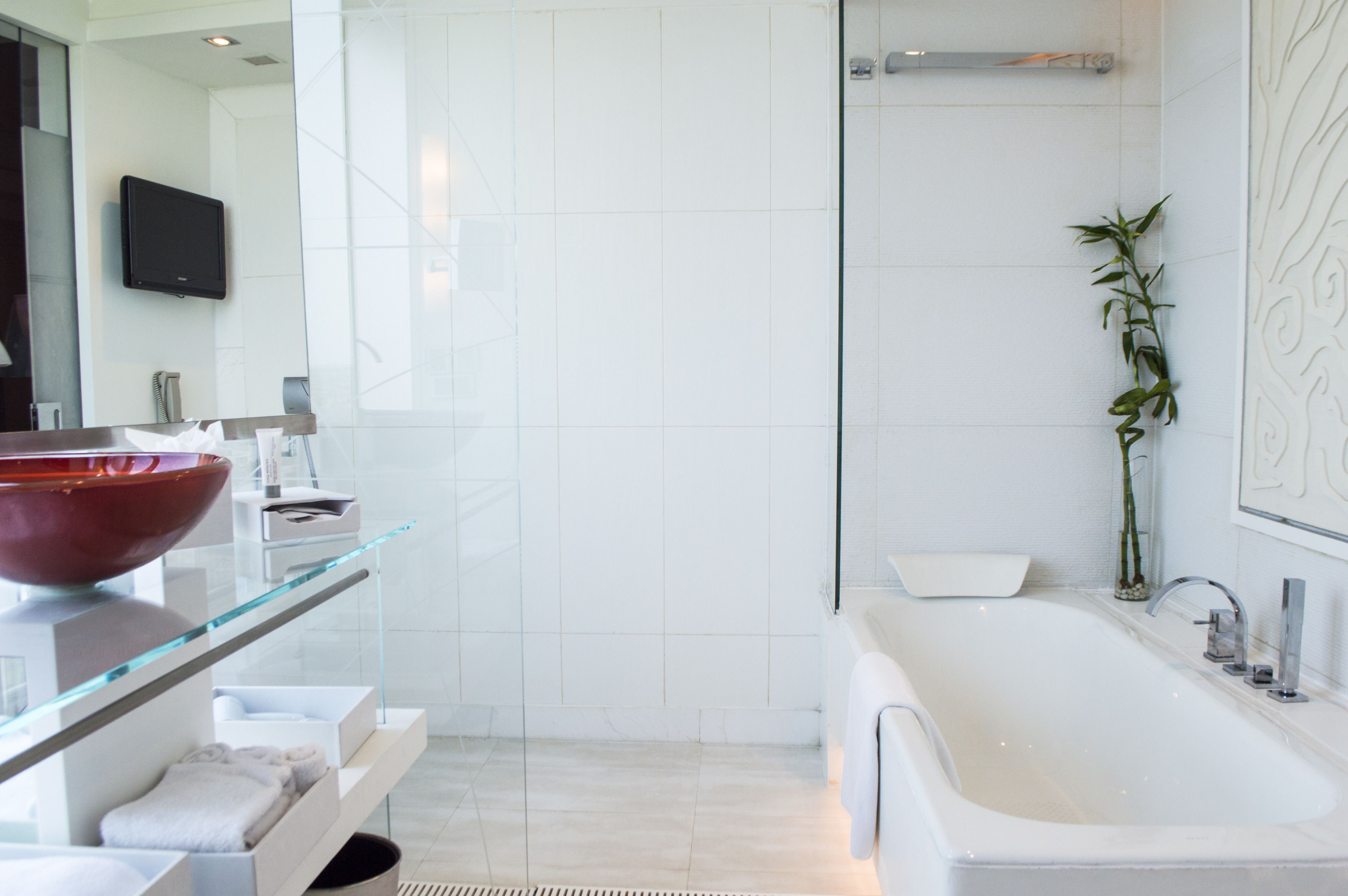 A modern bathroom with a large glass sink, a red bowl, a white bathtub, and a bamboo plant.
