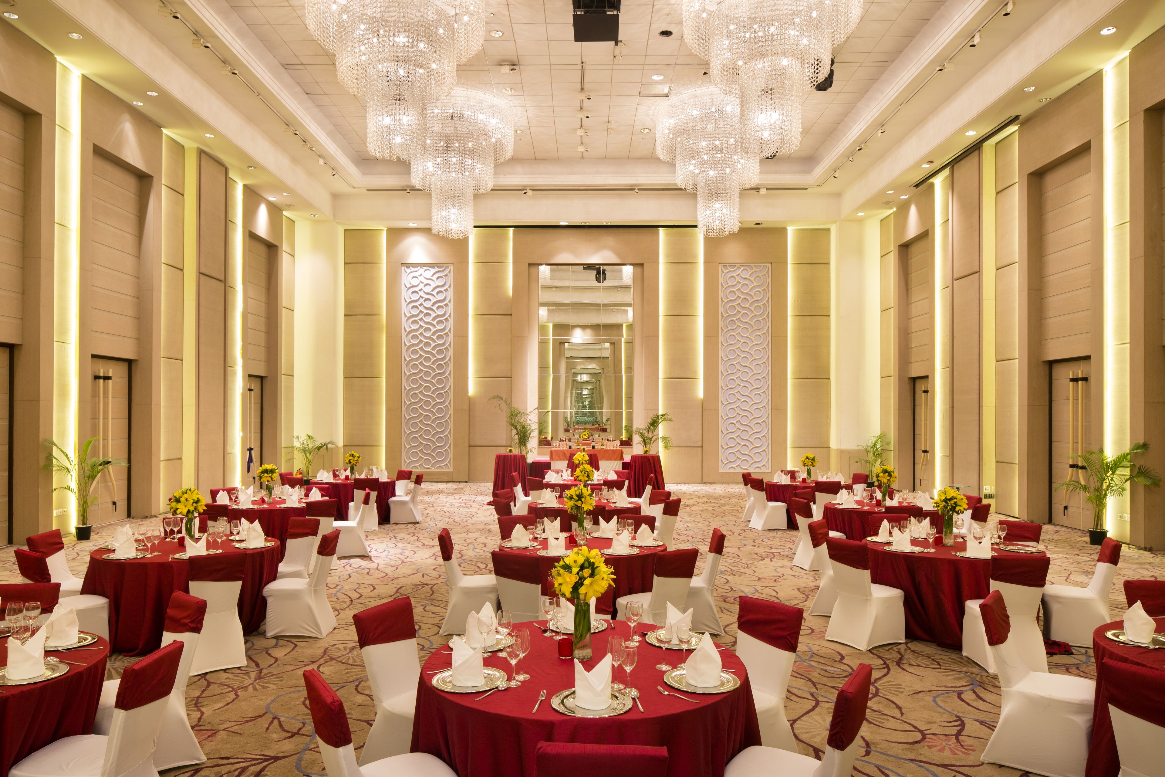A large banquet hall with round tables set for dining, featuring red tablecloths and white chairs.