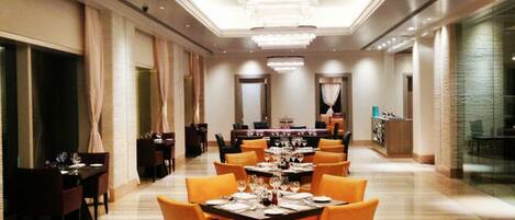 A spacious, well-lit dining area with multiple tables set for dining, featuring a modern chandelier and elegant decor.