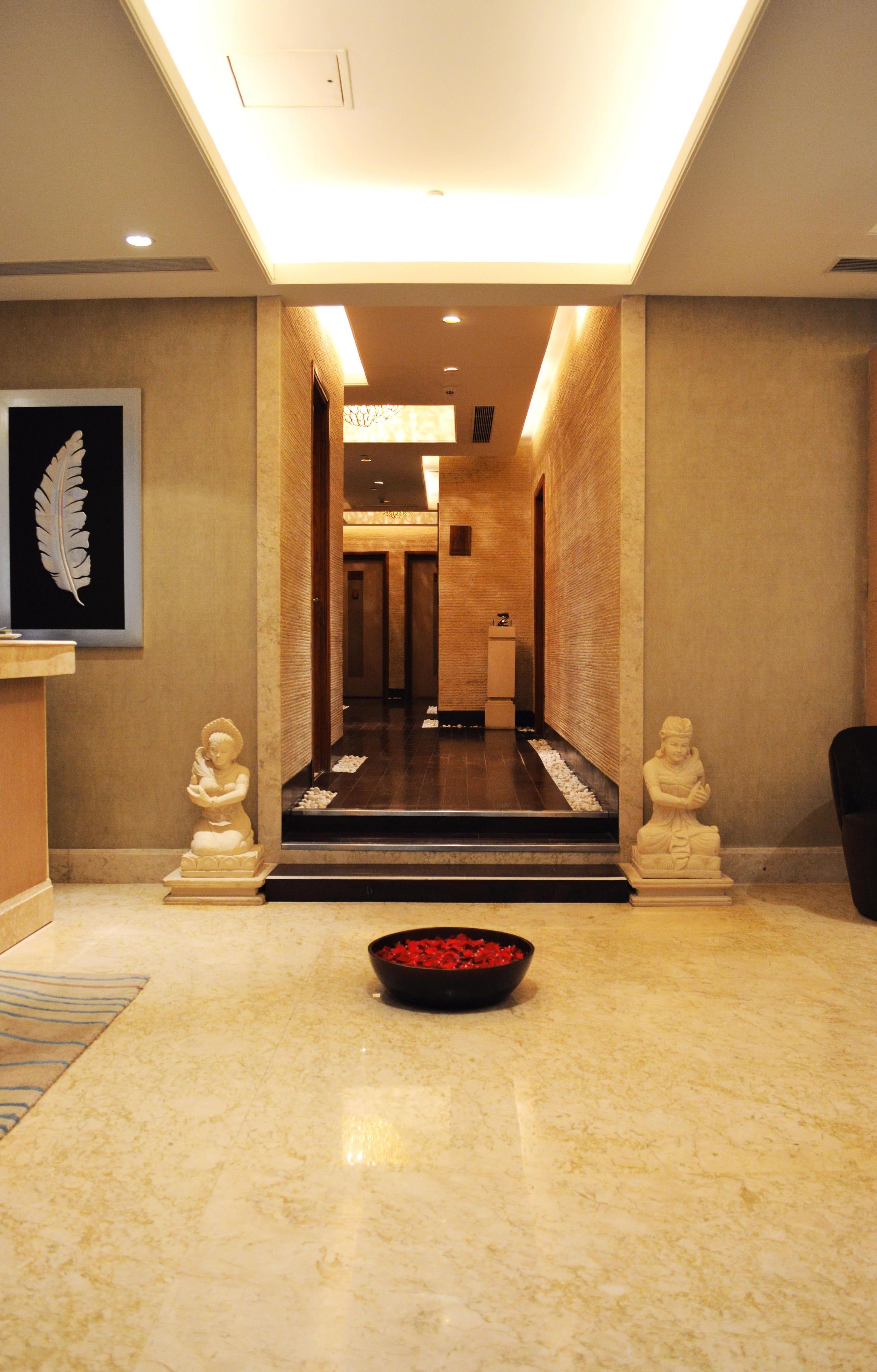 A hotel lobby with a marble floor, a reception desk, a framed artwork, and two statues.