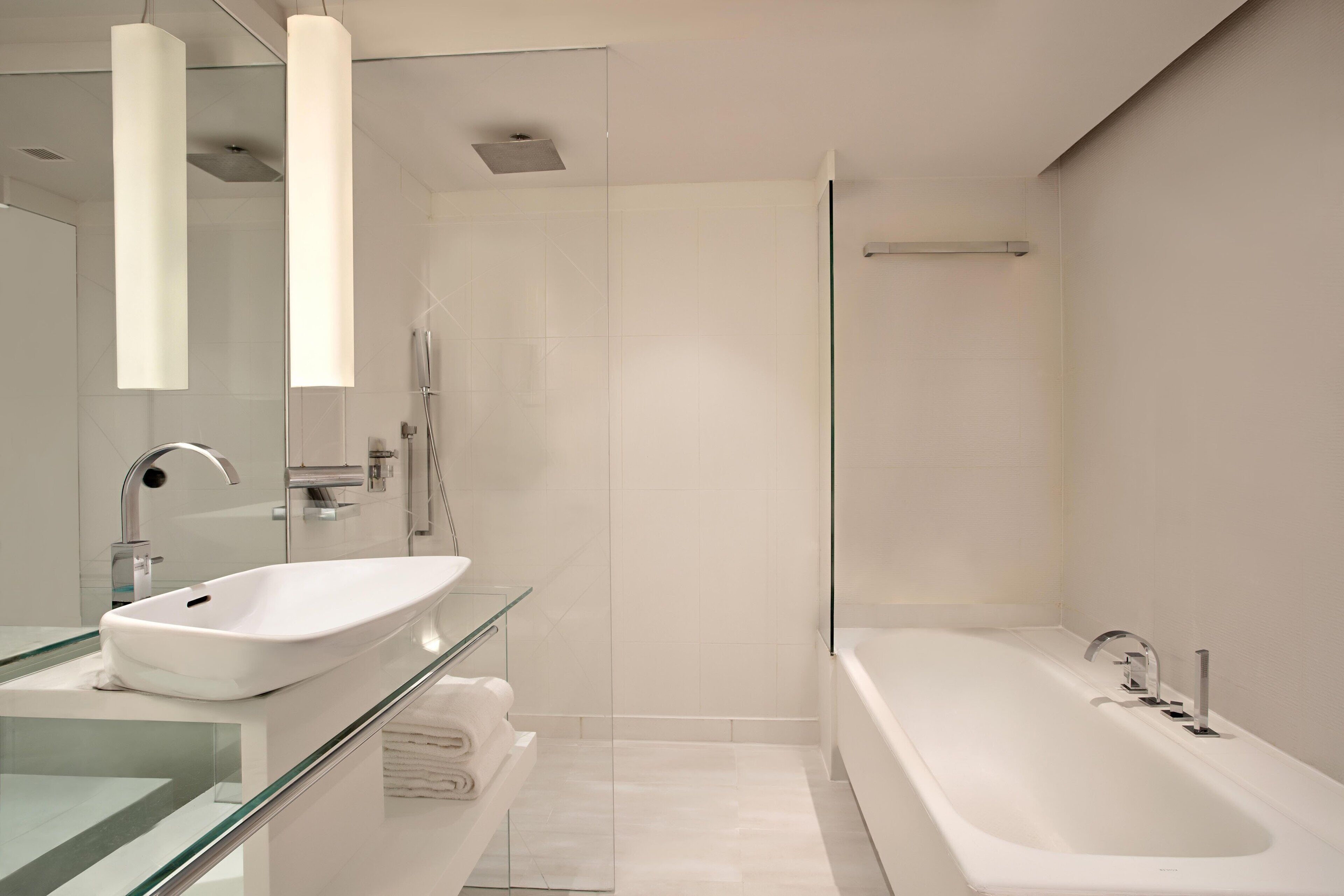 Un baño moderno con cabina de ducha de vidrio, una bañera blanca y un tocador con superficie de vidrio.