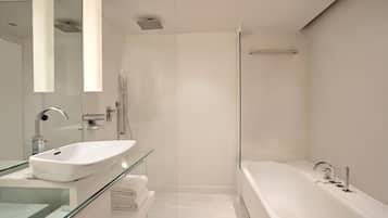 A modern bathroom with a glass shower enclosure, a white bathtub, and a glass-topped vanity.