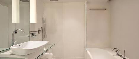 Un baño moderno con cabina de ducha de vidrio, una bañera blanca y un tocador con superficie de vidrio.