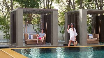 Relax by the serene pool surrounded by lush greenery and comfortable wicker lounge chairs.