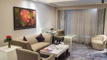 A modern hotel room with a sofa, armchair, desk, and a large window with curtains.