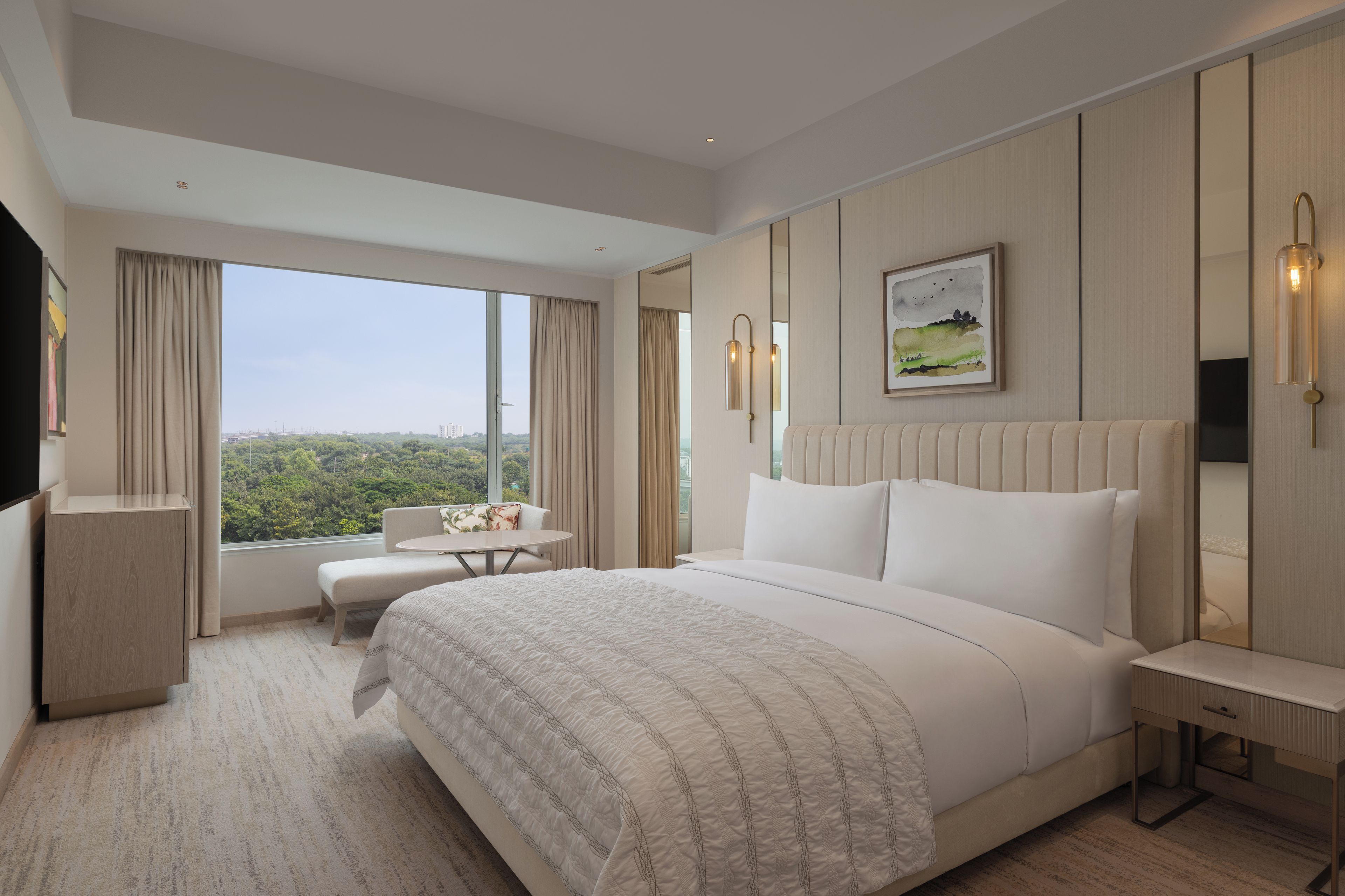 Ein Hotelzimmer mit einem großen Bett, einem Schreibtisch, einem Sessel und Blick auf die Stadt.