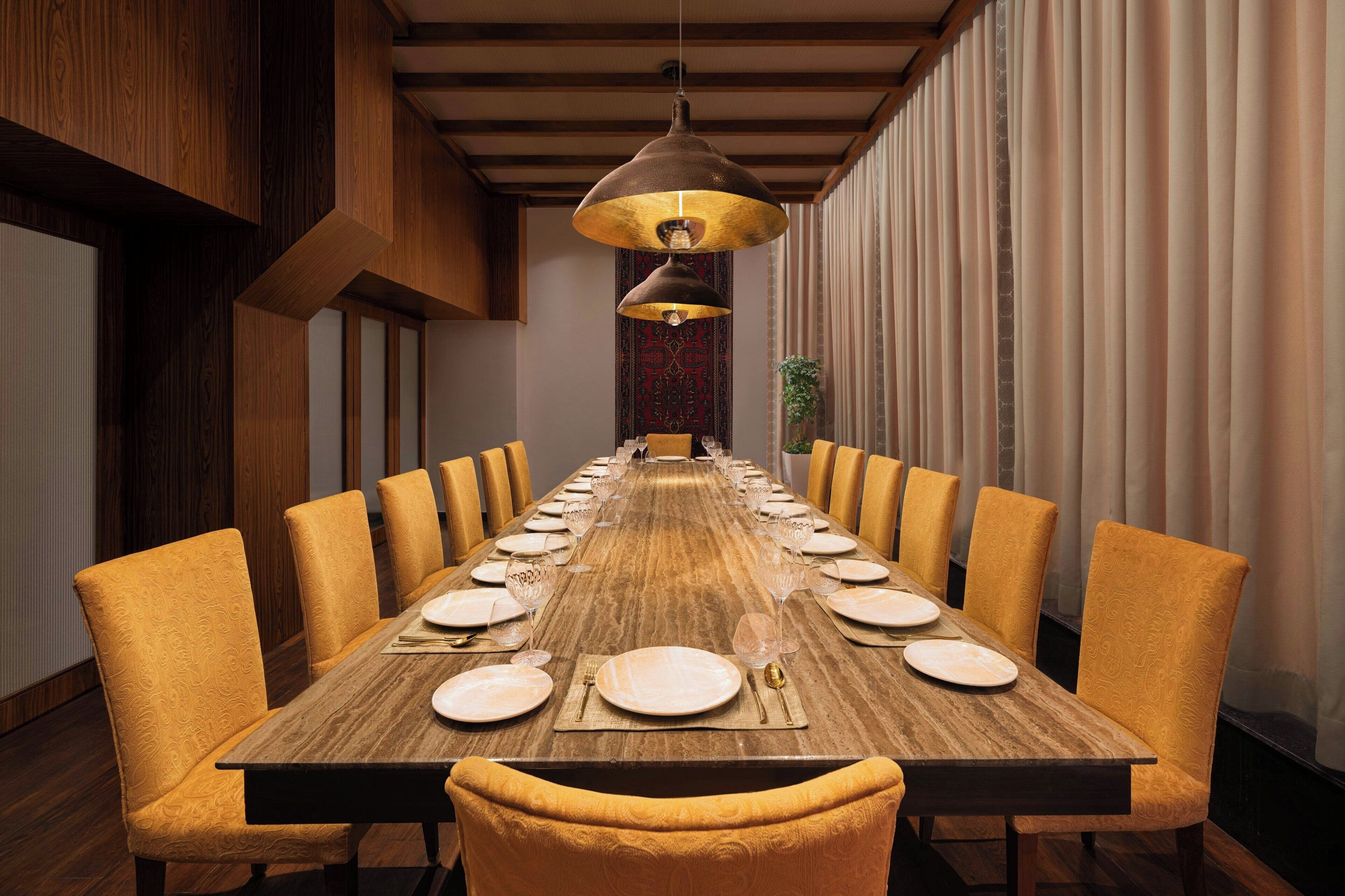 A long dining table with yellow upholstered chairs, set for a meal with plates, cutlery, and glasses.