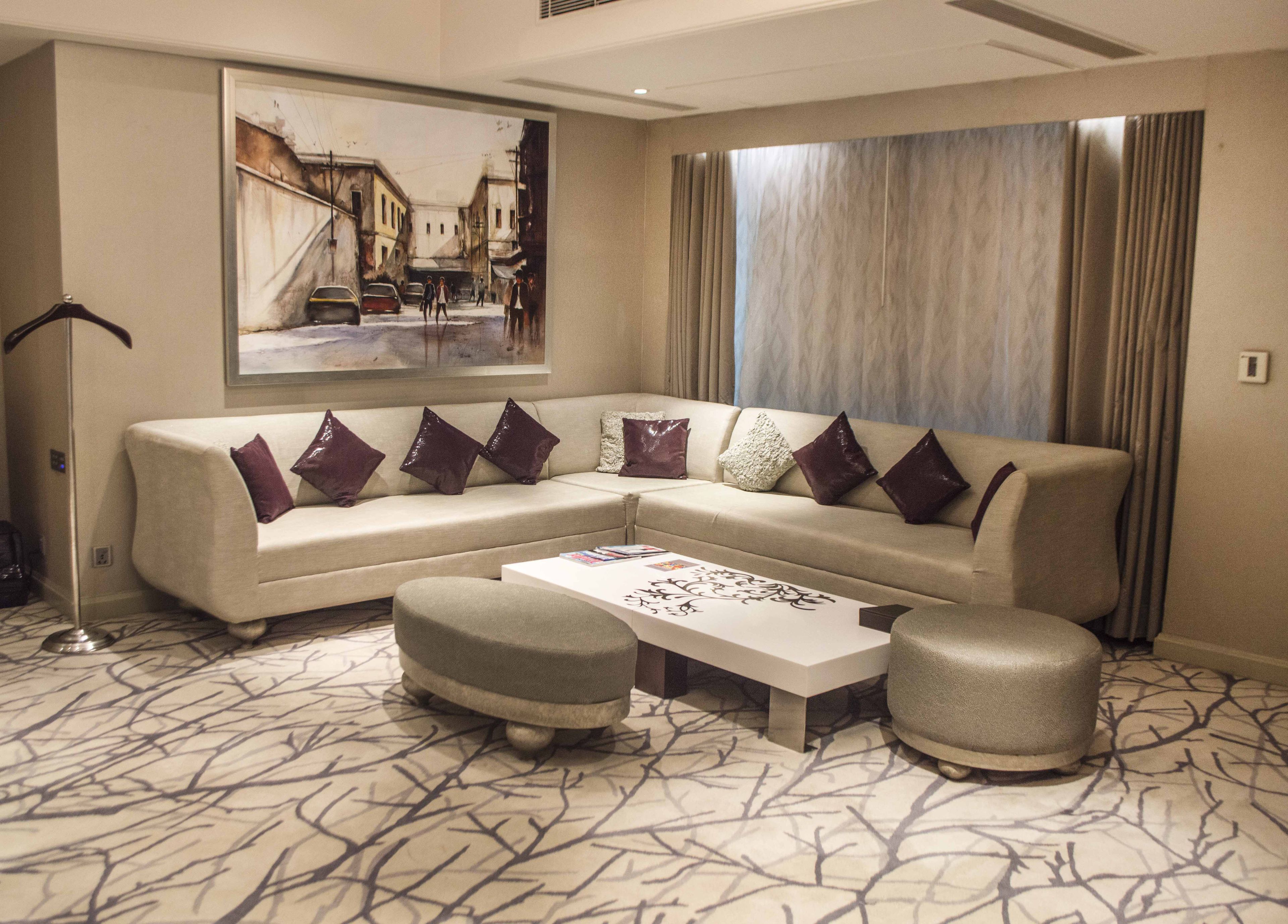A modern living room with a sectional sofa, ottomans, a coffee table, and a large painting on the wall.