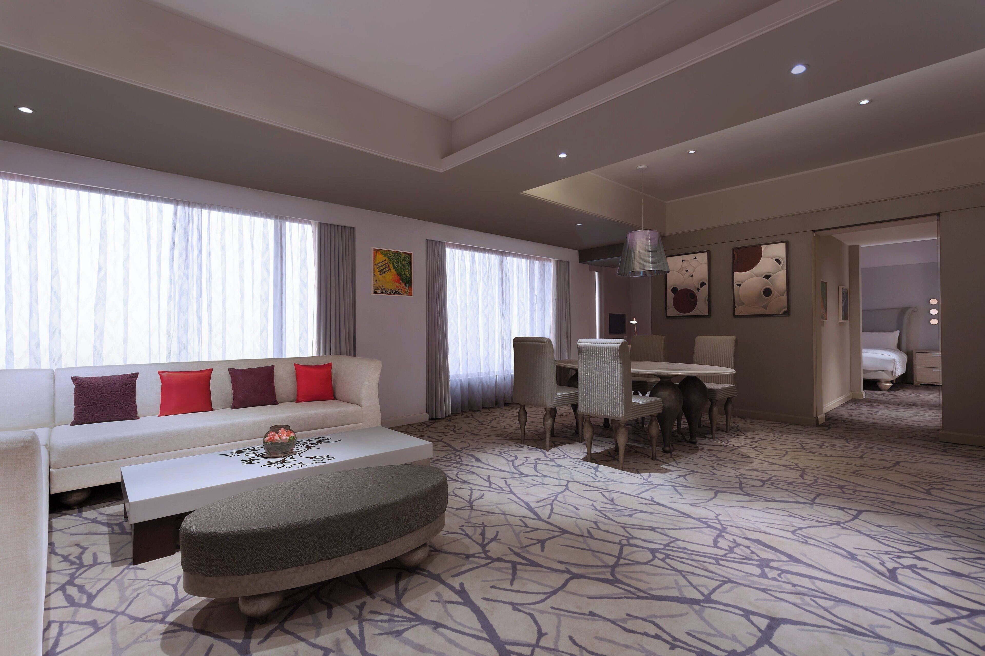 Een moderne hotelkamer met een bank, poef, eettafel, stoelen en kunstwerken aan de wanden.