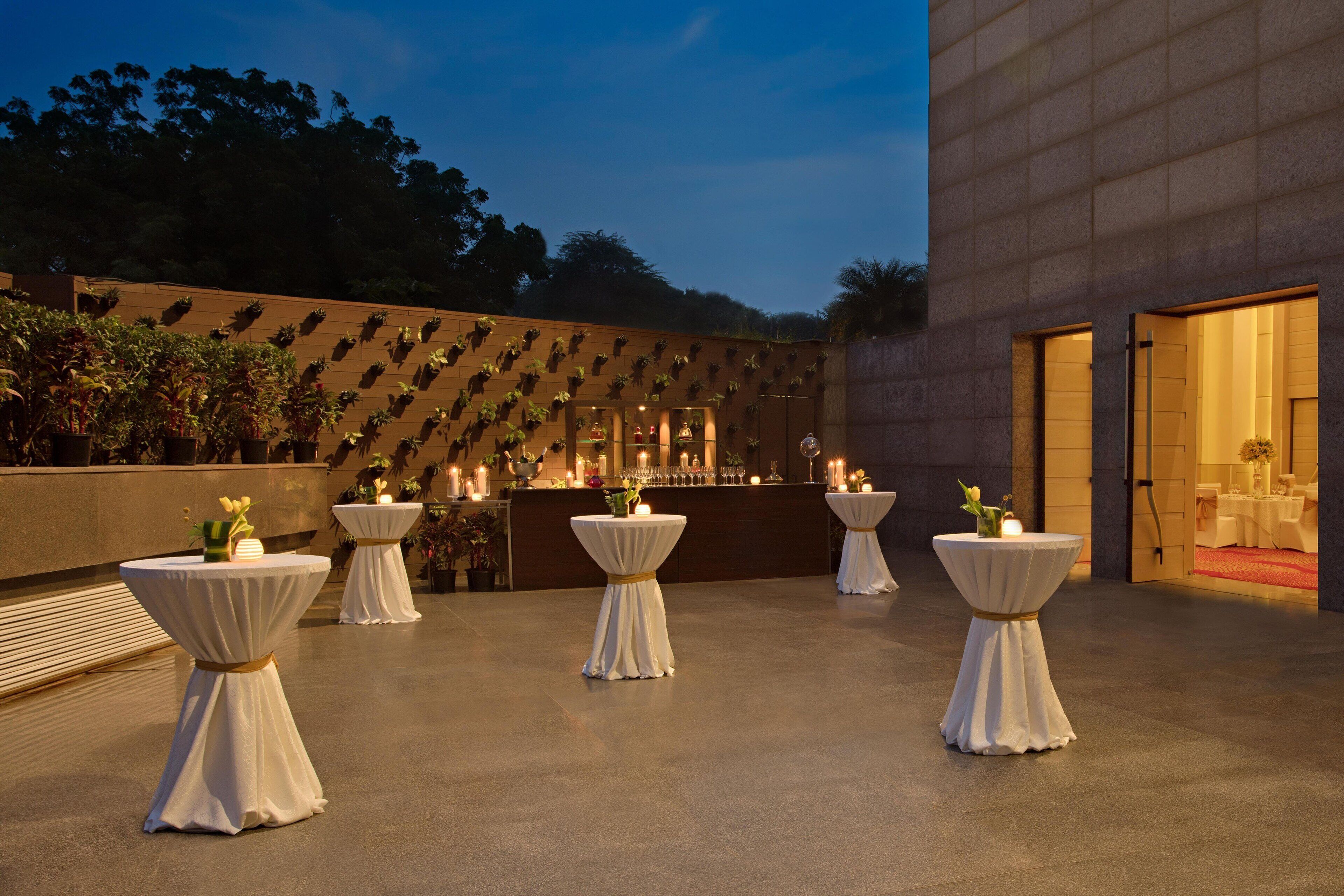 An outdoor patio area with round tables, a bar, and a wall adorned with plants.