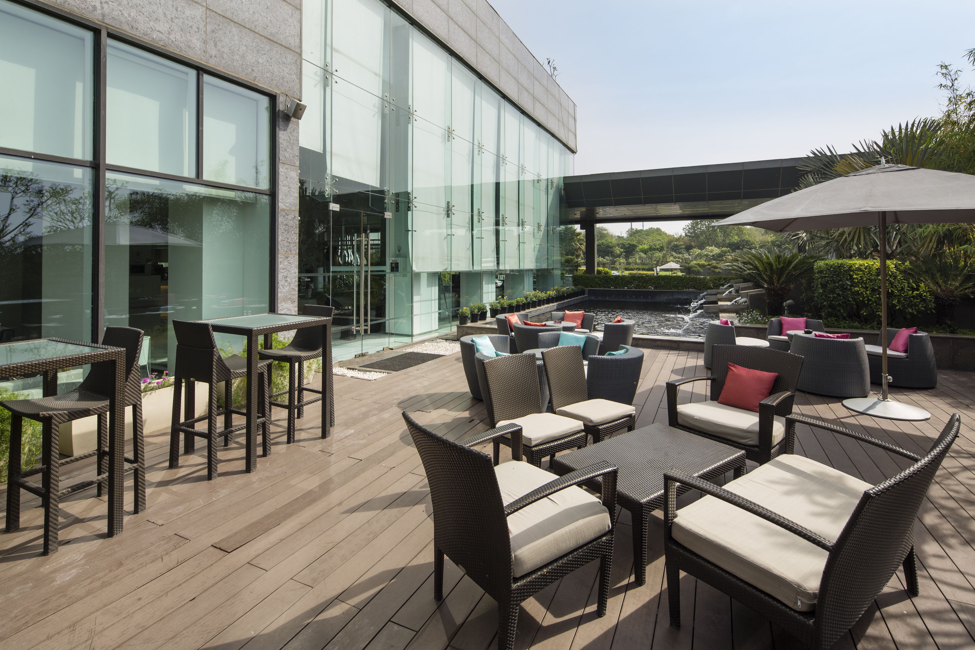 An outdoor patio with wicker furniture, a water feature, and a glass building in the background.