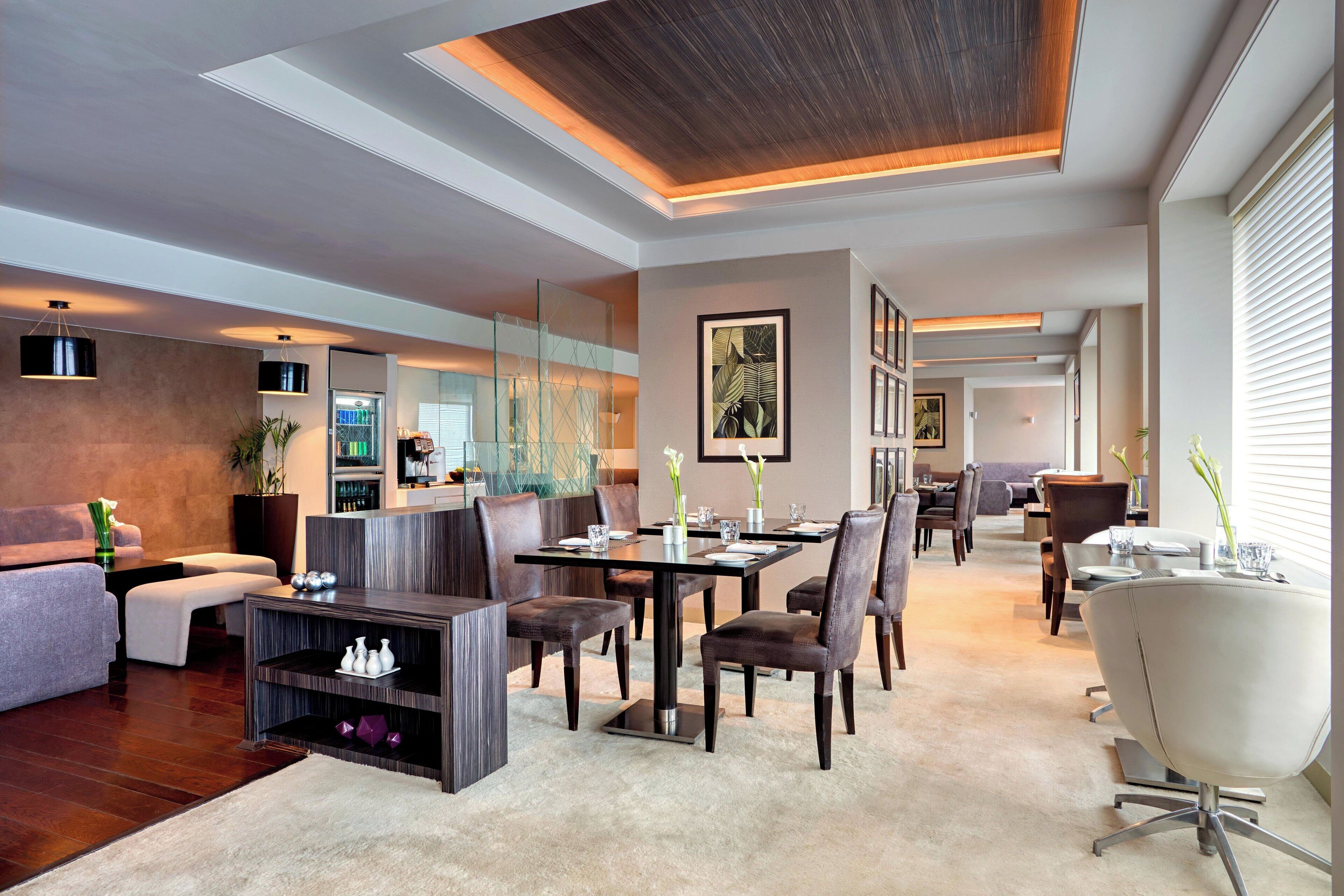 Un salon moderne avec un coin repas, caractérisé par un grand plafond en bois, des meubles aux couleurs sombres et une cloison en verre.
