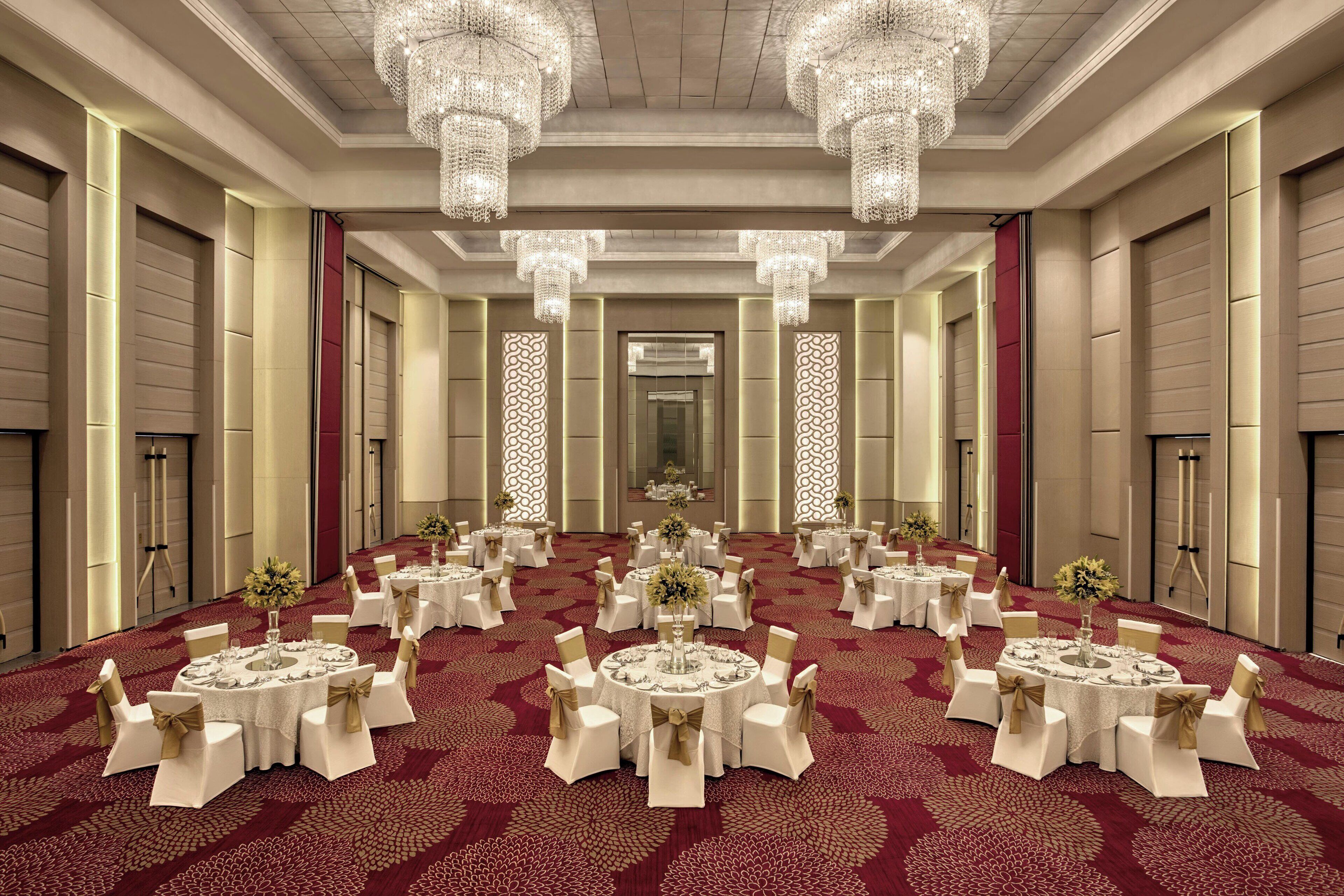 A spacious banquet hall with multiple round tables, each set with white tablecloths and gold sashes, surrounded by white chairs.