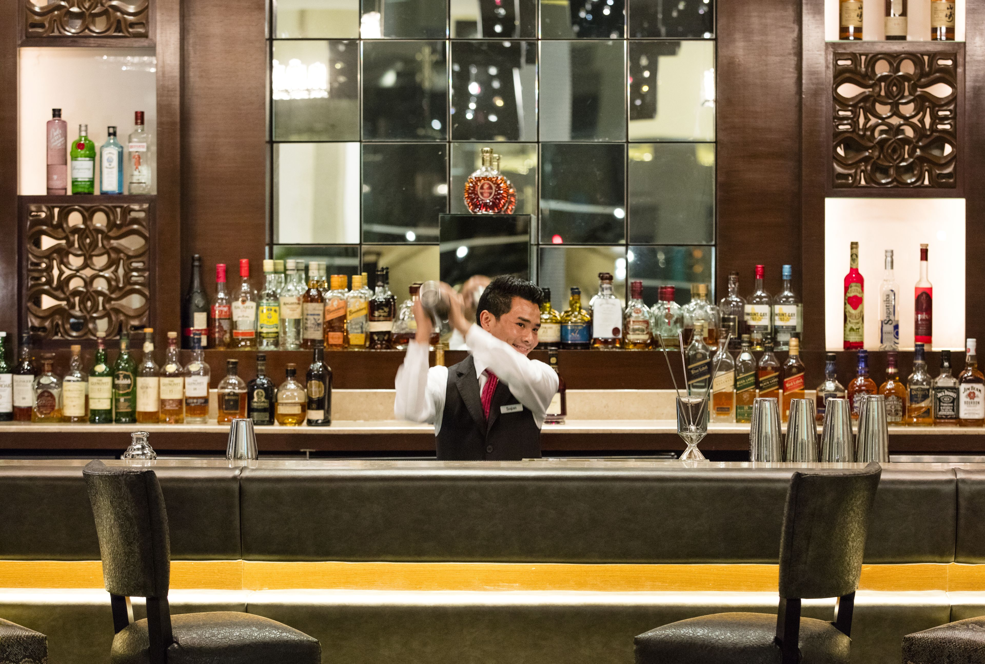 A bar area with a bartender, shelves of liquor bottles, and a large mirror reflecting the interior.