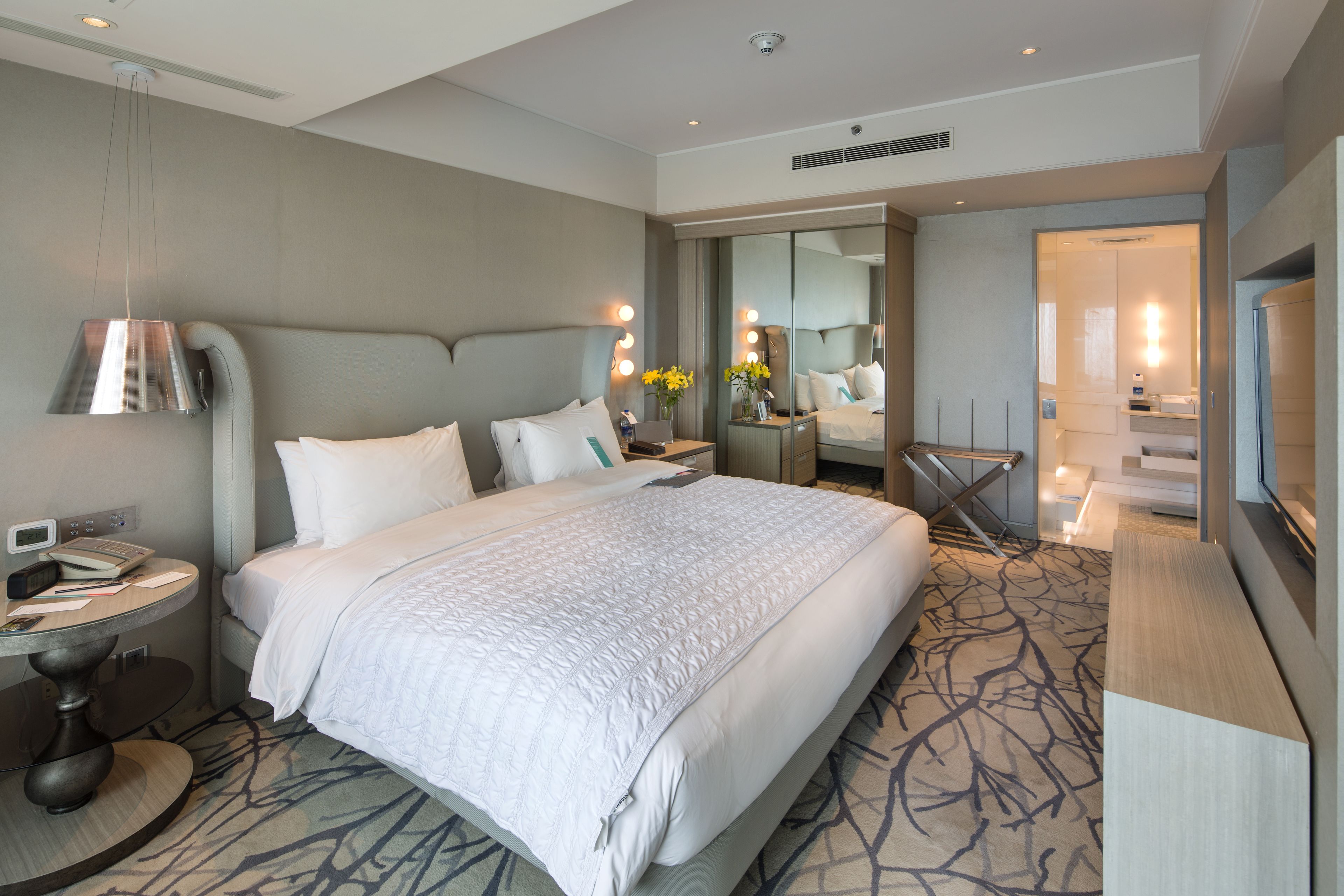 Ein modernes Hotelzimmer mit einem großen Bett, Nachttischen, einem Schreibtisch und einem Fernseher.