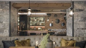 A modern bar area with a wooden ceiling, stone walls, and a bar counter with various bottles. There is a seating area with a wooden table and cushions. - Hotel Sonnenhof (Gerlos)