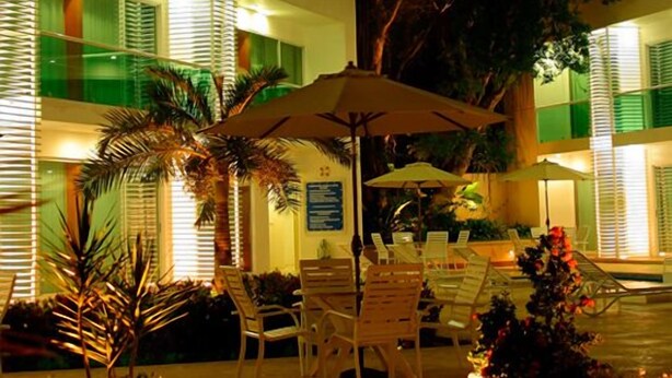 Un'area salotto esterna con tavoli e sedie, circondata da palme e da una piscina.