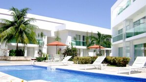 Un hotel moderno con piscina, lettini e palme.