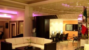 Una hall d'hotel moderna con un divano bianco, un tavolino da caffè e una zona pranzo con sedie e un tavolo.