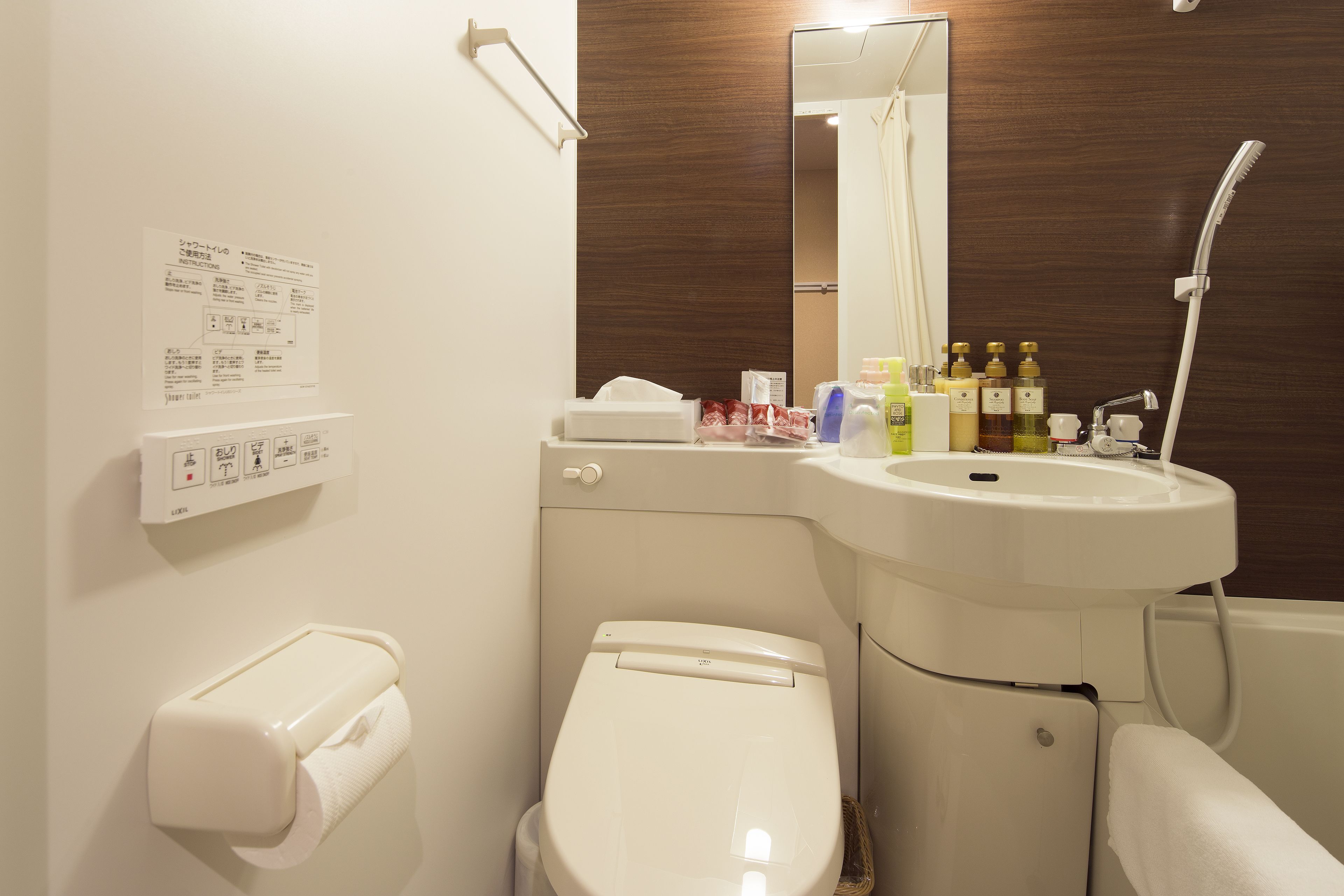 A bathroom with a toilet, sink, and shower. There are toiletries on the sink counter.
