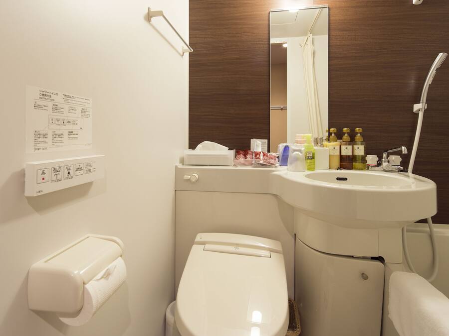 A bathroom with a toilet, sink, and shower. There are toiletries on the sink counter.