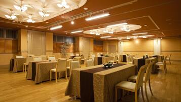 A conference room with multiple tables and chairs, ceiling lights, and a decorative plant.