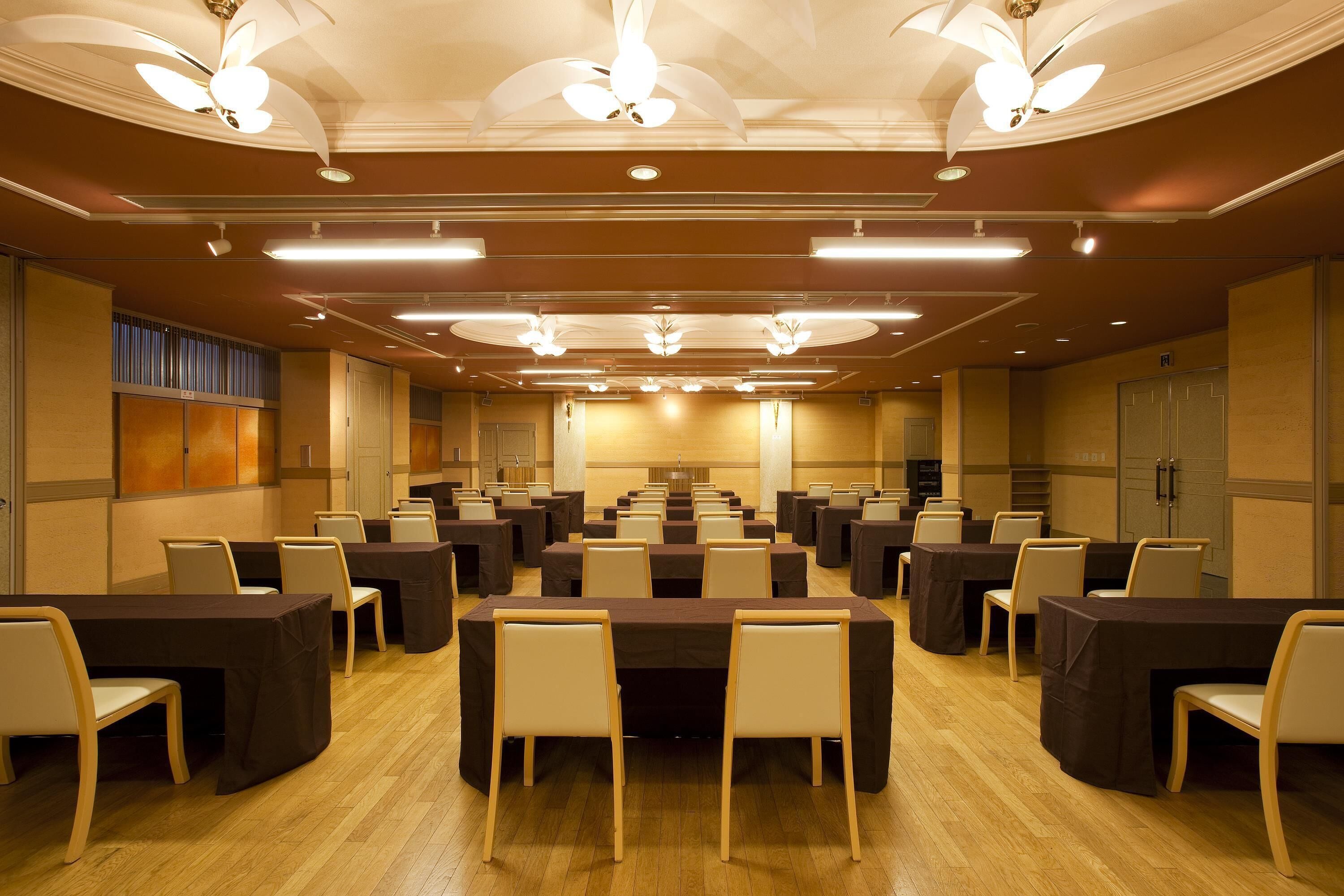 A conference room with multiple tables and chairs, ceiling fans, and recessed lighting.