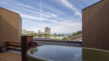 Un jacuzzi en una terraza de madera con vista a un lago y edificios al fondo.