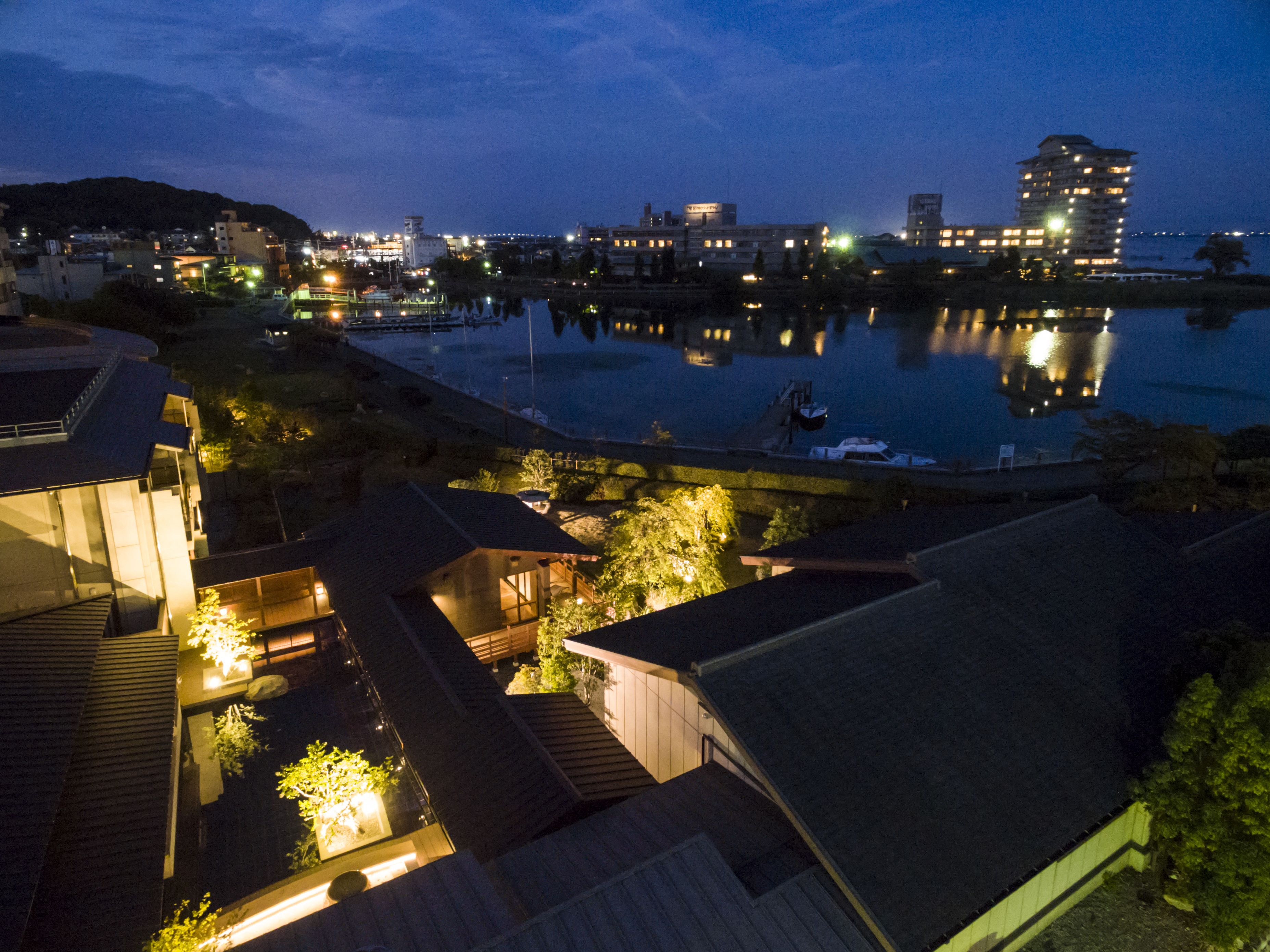 A traditional Japanese-style building with a view of a calm river and city lights in the background.